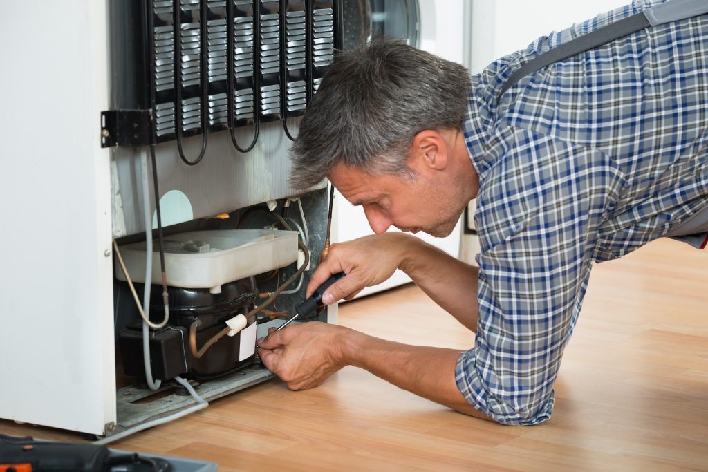 Cropped image of serviceman working on fridge with screwdriver at home